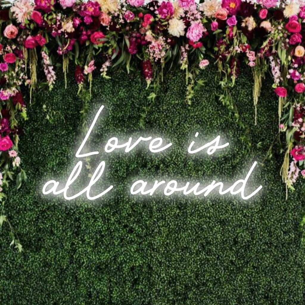 Placa de neon LED com a frase "O amor está em toda parte" em cores vibrantes, ideal para adicionar aconchego e positividade a qualquer espaço.