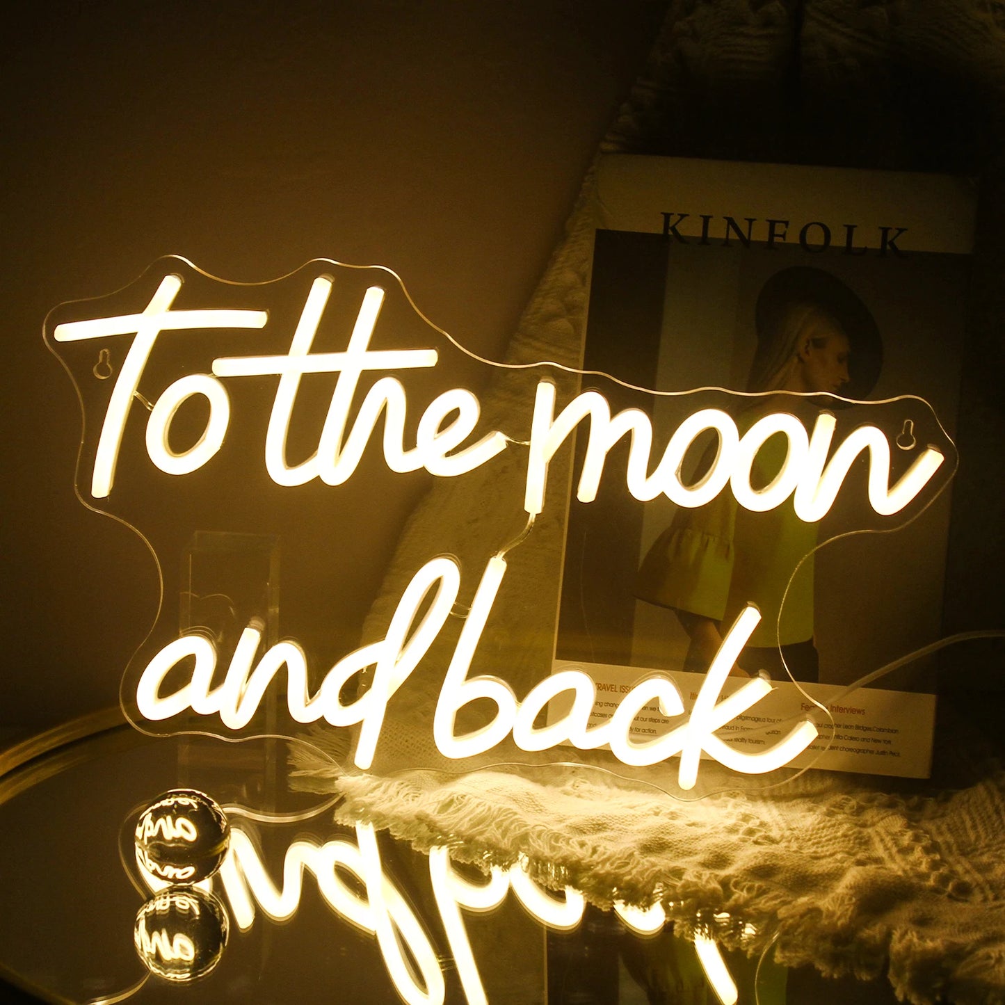 A imagem apresenta uma placa de LED neon feita à mão exibindo a frase "To The Moon And Back" em letras cursivas elegantes.