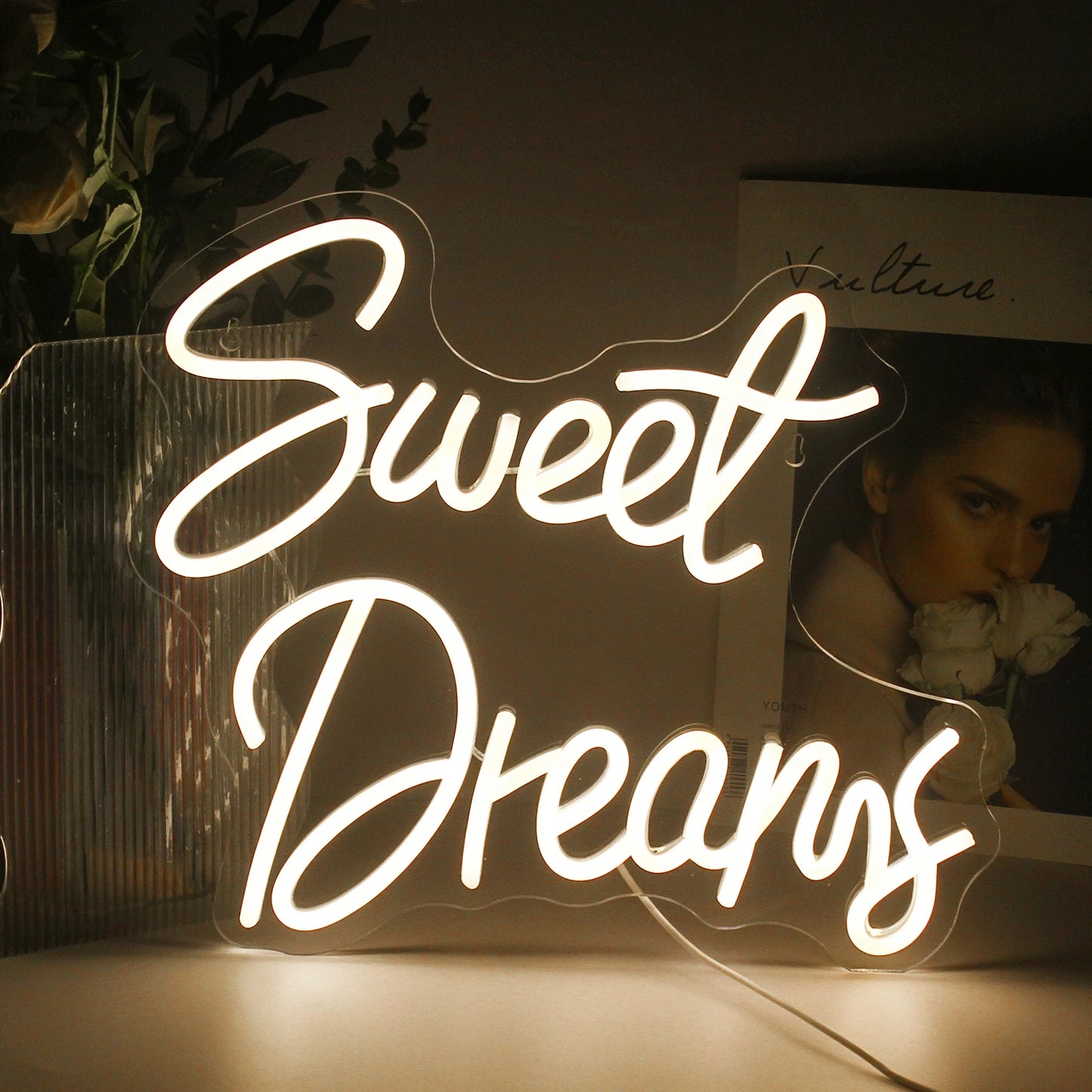 A imagem mostra uma placa de LED neon estilosa e vibrante exibindo as palavras "Sweet Dreams" em uma fonte fluida e cursiva.