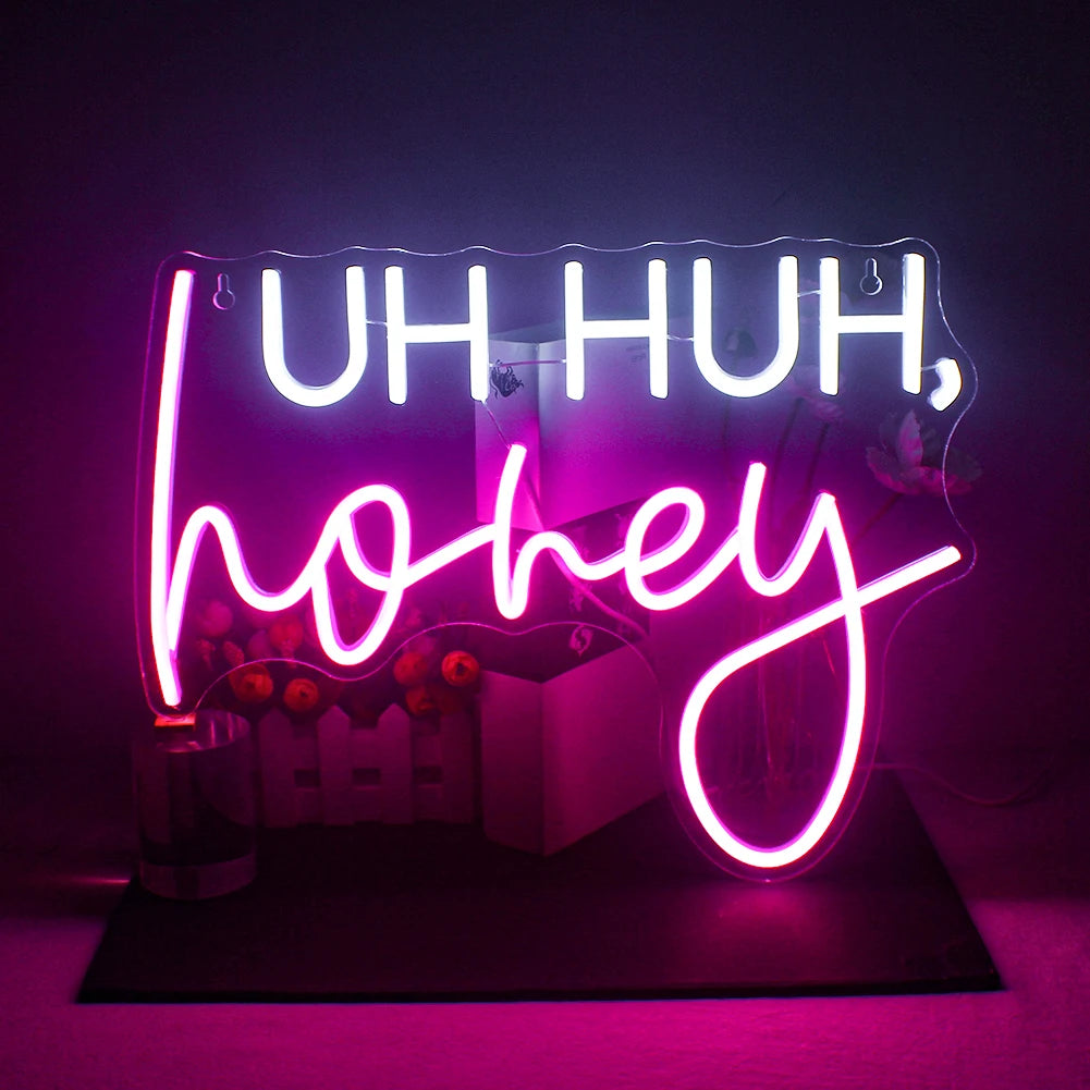 A imagem apresenta uma vibrante placa de LED neon feita à mão exibindo a frase "Uh Huh" em uma escrita cursiva animada.