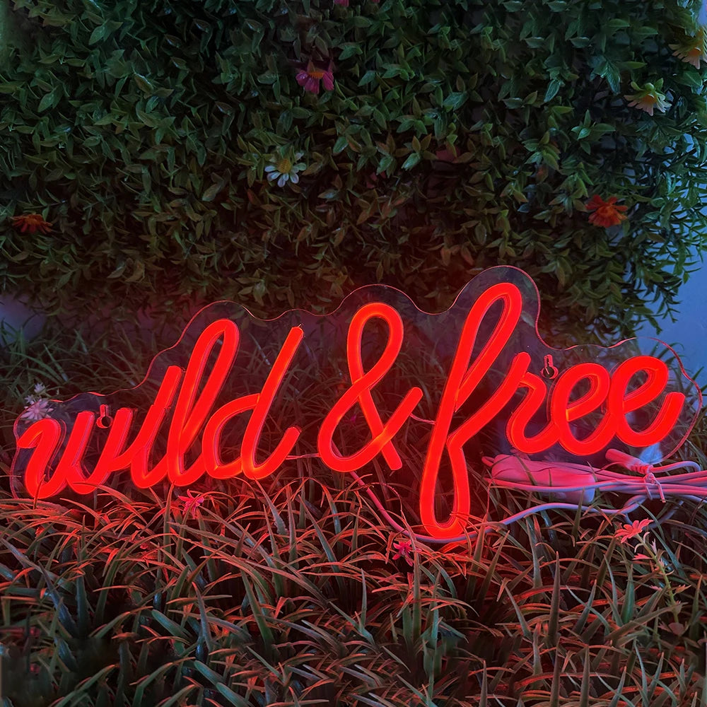 A imagem apresenta uma vibrante placa de LED neon exibindo as palavras "Wild & Free" em uma fonte cursiva e estilosa.