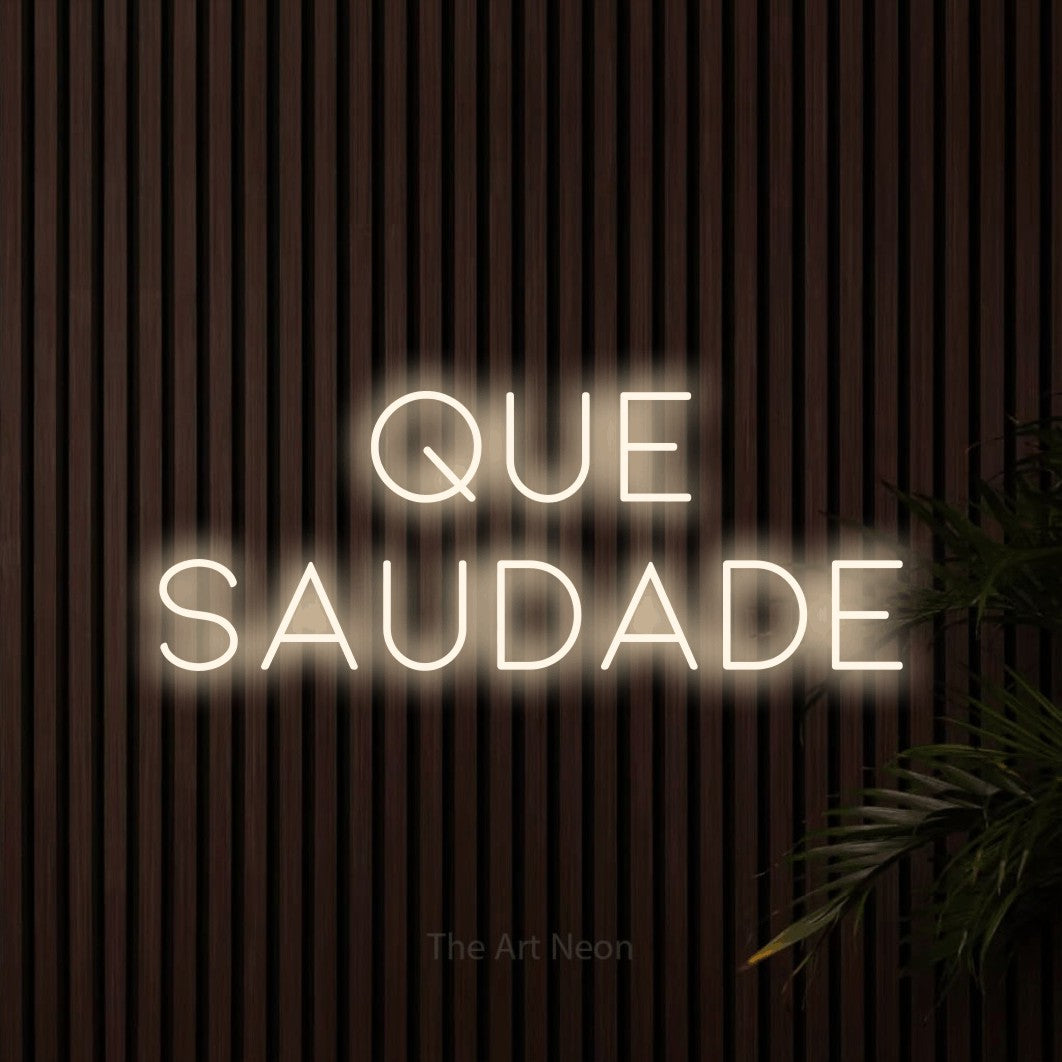 LED neon sign reading “que saudade”, arranged in 2 lines.
