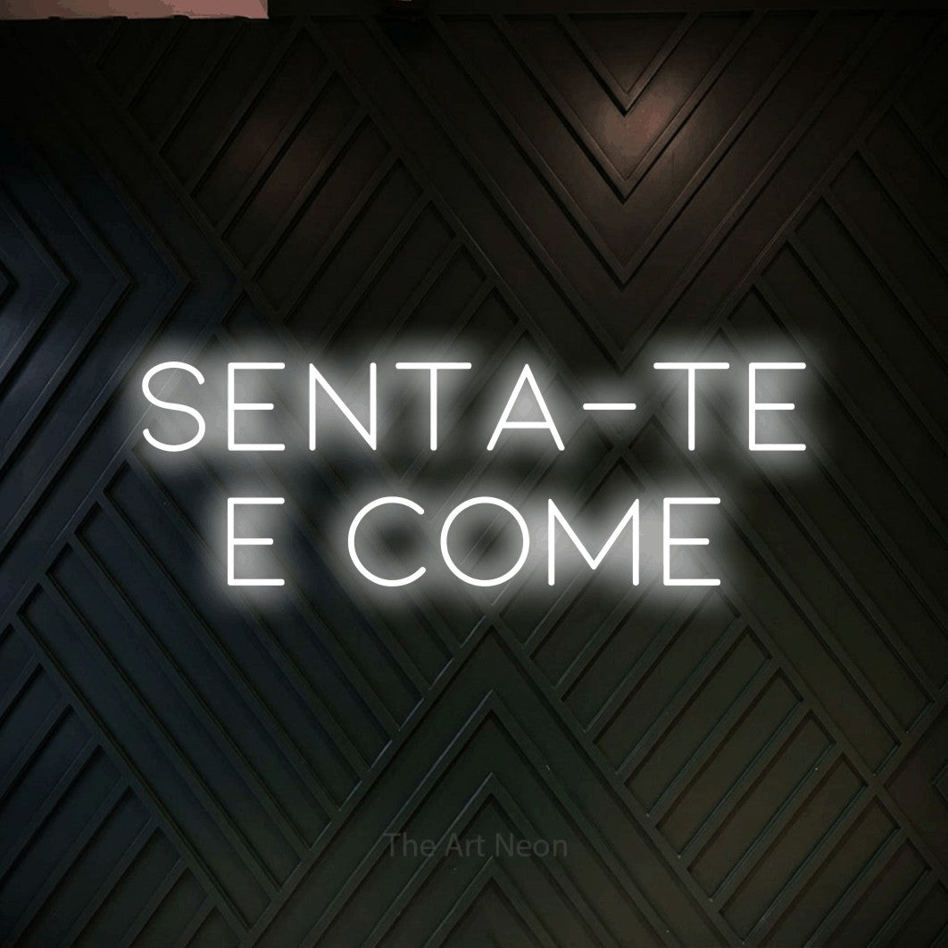 LED neon sign reading “senta-te e come”, arranged in 2 lines.