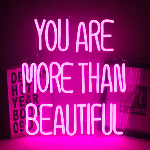 A imagem apresenta um letreiro de LED neon vibrante exibindo a frase "Você é mais que bonita".