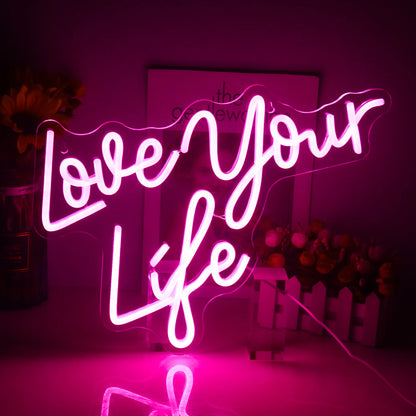 A brightly illuminated LED neon sign displaying the words "Love Your Life" in a stylish, cursive script.
