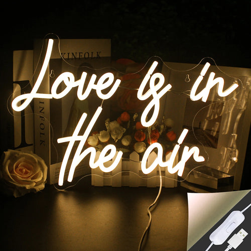 A imagem apresenta uma vibrante e estilosa placa de LED neon que diz "O amor está no ar" em uma elegante letra cursiva.