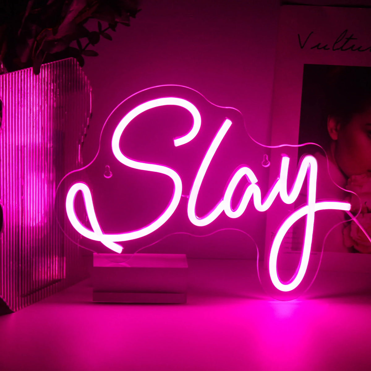 A imagem apresenta uma placa de LED neon vibrante e feita à mão exibindo a palavra "Slay" em uma fonte cursiva elegante.