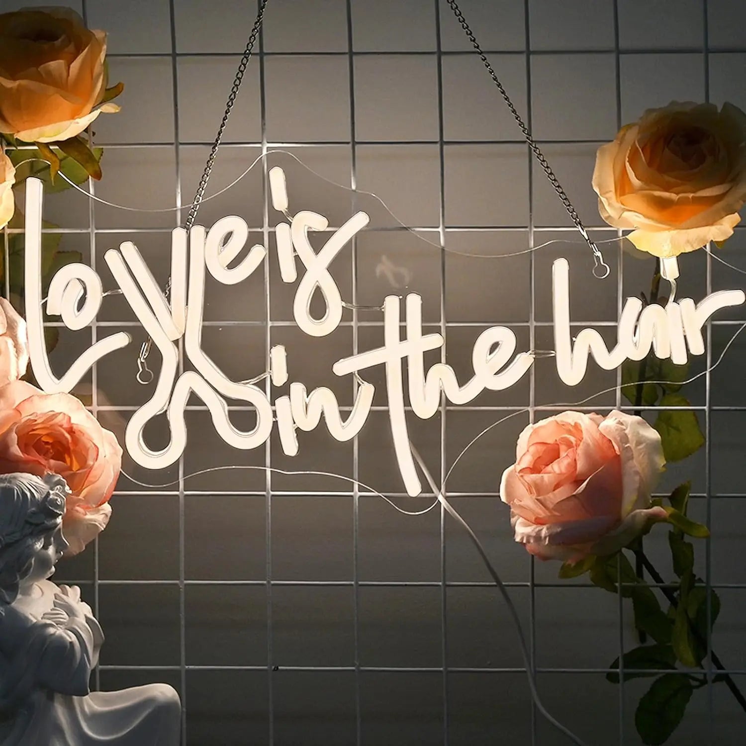 The image features a vibrant, handmade LED neon sign spelling out the phrase "Love is in the Hair.