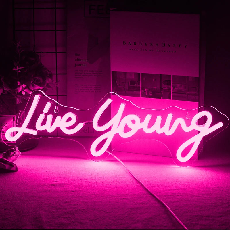 The image displays a vibrant handmade LED neon sign featuring the phrase "Live Young" in a lively, cursive script.