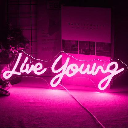 The image displays a vibrant handmade LED neon sign featuring the phrase "Live Young" in a lively, cursive script.