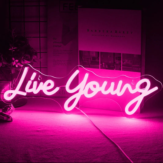 The image displays a vibrant handmade LED neon sign featuring the phrase "Live Young" in a lively, cursive script.