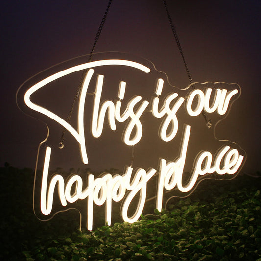 The image features a vibrant LED neon sign displaying the words "This is our happy place" in cursive script.