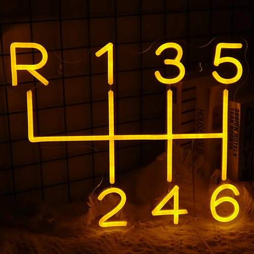A imagem exibe uma placa de LED neon feita à mão, em formato de caixa de câmbio de carro.