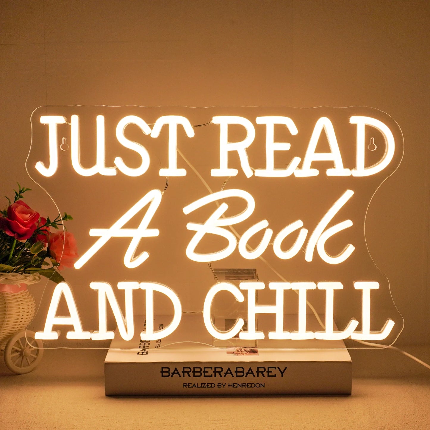 The image features a vibrant LED neon sign that spells out the phrase "Just Read A Book And Chill.