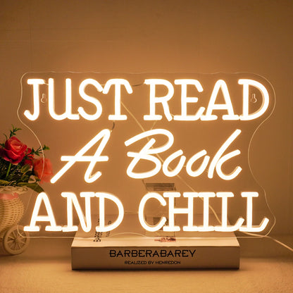 The image features a vibrant LED neon sign that spells out the phrase "Just Read A Book And Chill.