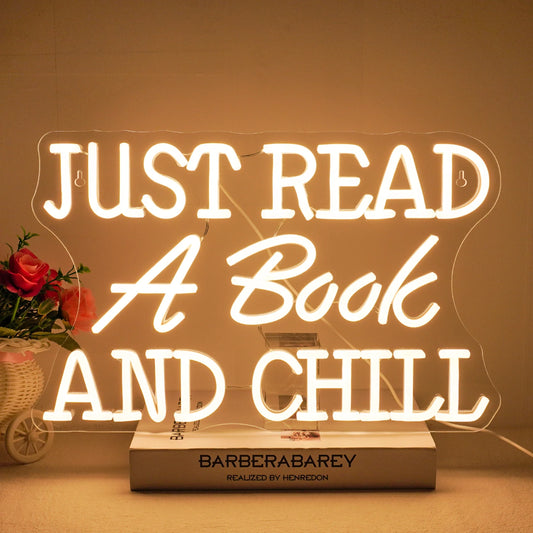 The image features a vibrant LED neon sign that spells out the phrase "Just Read A Book And Chill.
