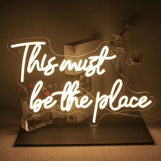 The image displays a vibrant LED neon sign that reads "This must be the place" in cursive script.