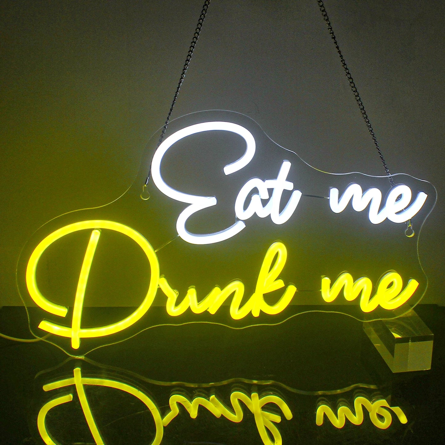 The image features a vibrant LED neon sign displaying the words "Eat Me Drink Me" in a whimsical, cursive font.