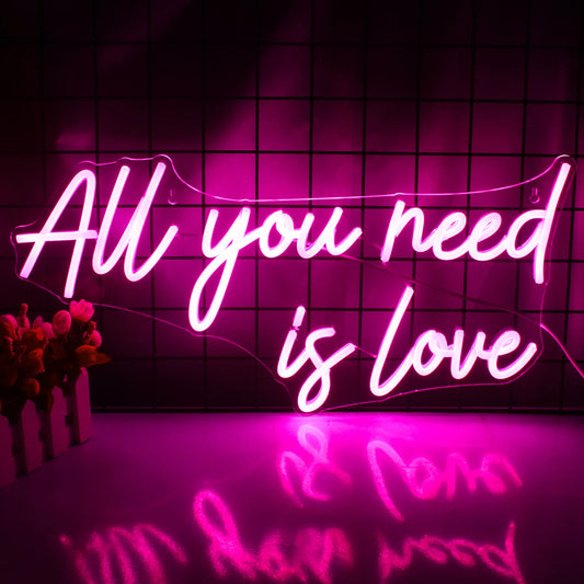The image displays a vibrant LED neon sign with the phrase "All You Need is Love" in elegant, cursive lettering.