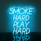 A imagem mostra uma placa de LED neon vibrante que diz "Smoke Hard Play Hard" em letras maiúsculas e em negrito.