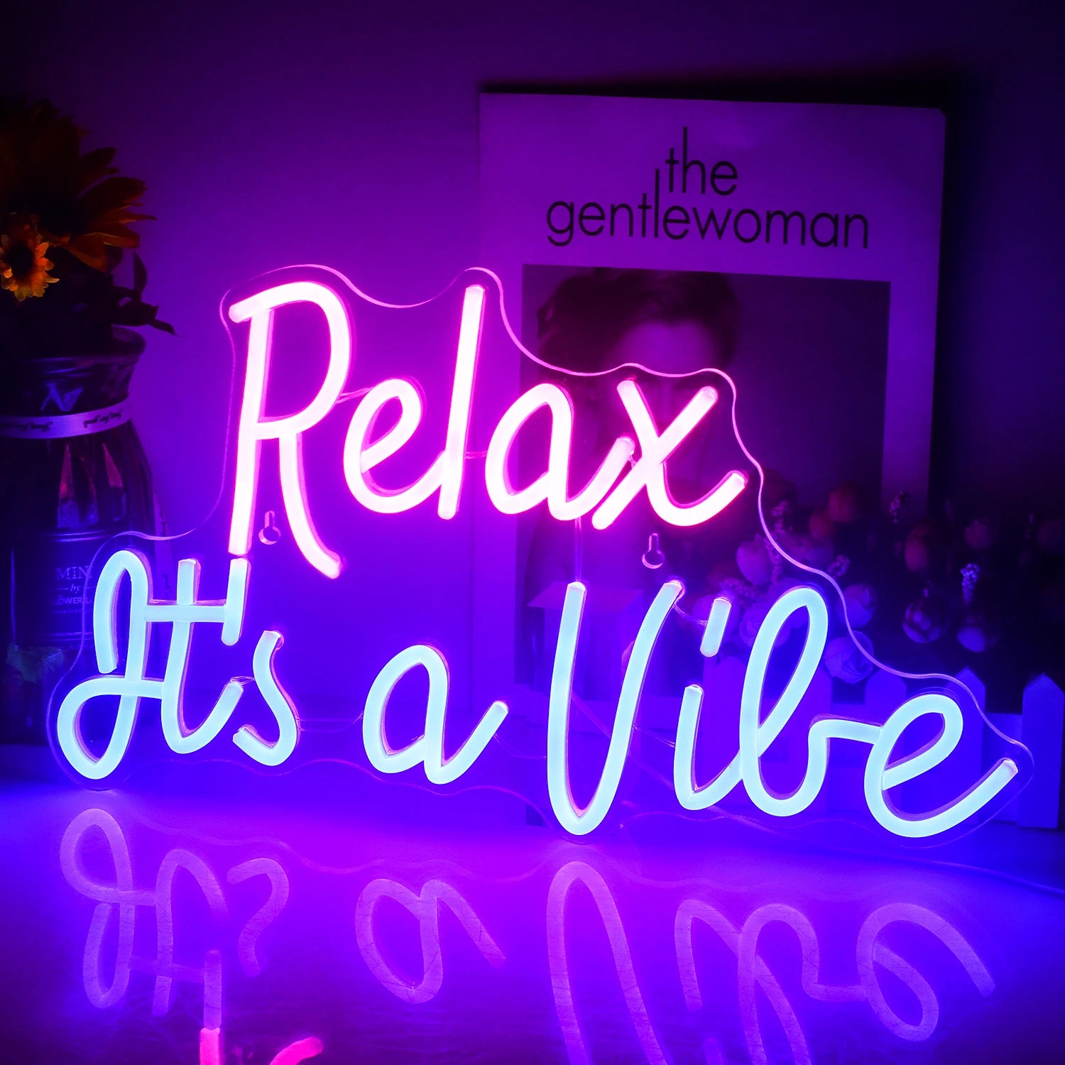 The image shows a vibrant LED neon sign displaying the phrase "Relax It's a Vibe" in a stylish, cursive font.