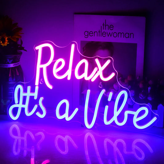 The image shows a vibrant LED neon sign displaying the phrase "Relax It's a Vibe" in a stylish, cursive font.