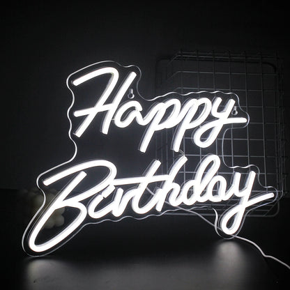 A vibrant "Happy Birthday" LED neon sign glowing warmly against a dark background.