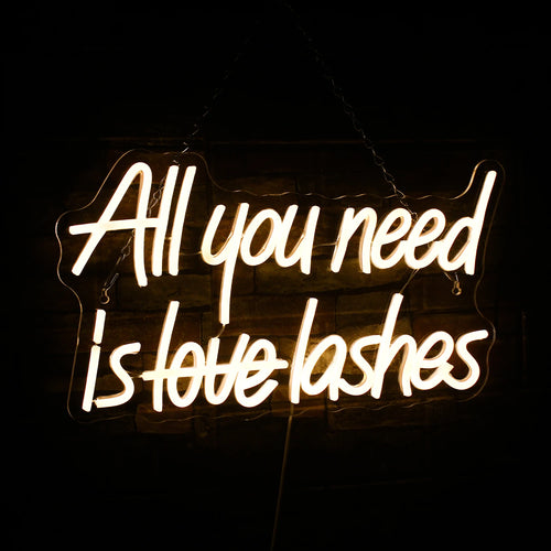 A imagem apresenta um letreiro de LED neon vibrante exibindo a frase "All You Need is Lashes" em letras cursivas elegantes.