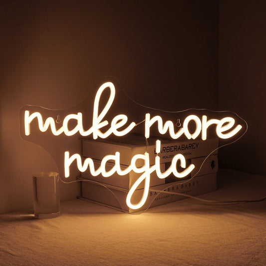 A vibrant "Make More Magic" LED neon sign in a lively mix of colors is mounted against a sleek, dark background.