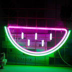 Um letreiro de LED neon vibrante em formato de fatia de melancia, com cores rosa e verde brilhantes.