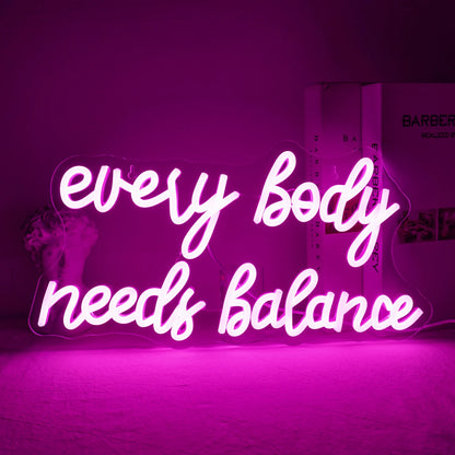 The image displays a vibrant "Every Body Needs Balance" LED neon sign.