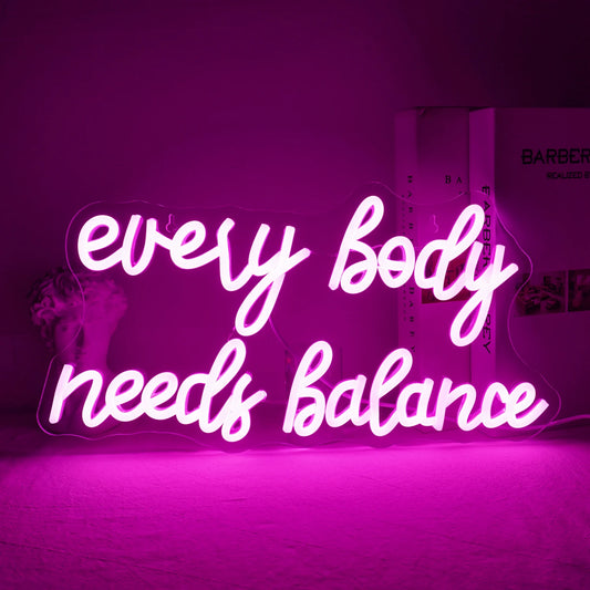 The image displays a vibrant "Every Body Needs Balance" LED neon sign.