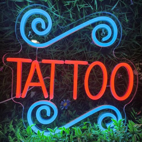 Uma placa de LED neon iluminada soletra a palavra "TATTOO" em letras maiúsculas e em negrito.