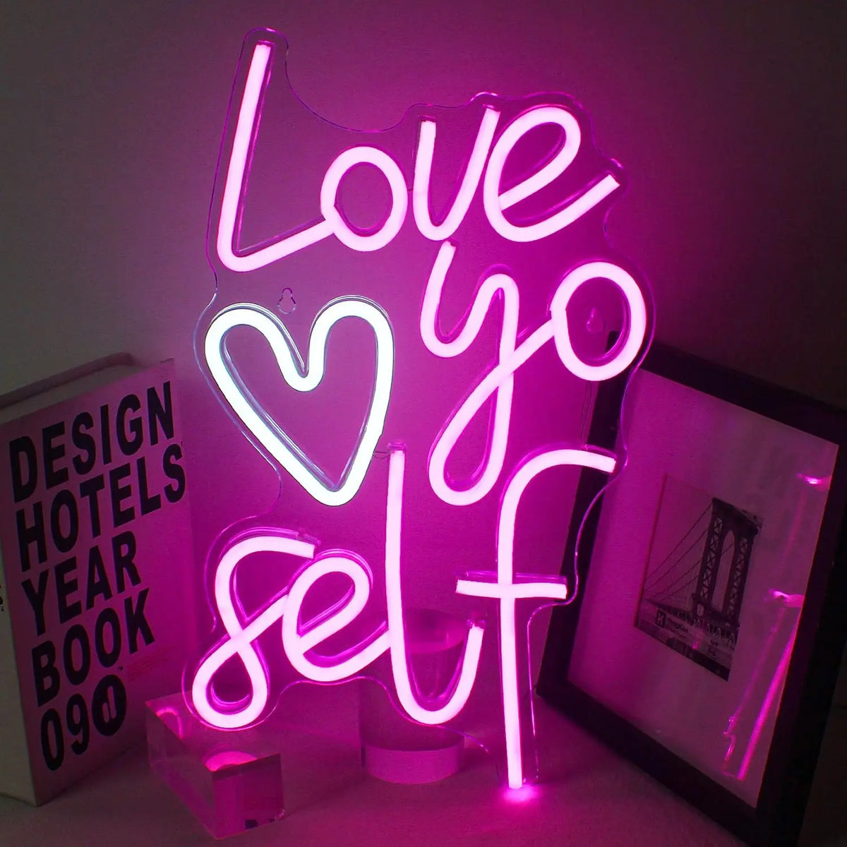Uma vibrante placa de LED neon "Love Yo Self" é exibida sobre um fundo escuro e simples.