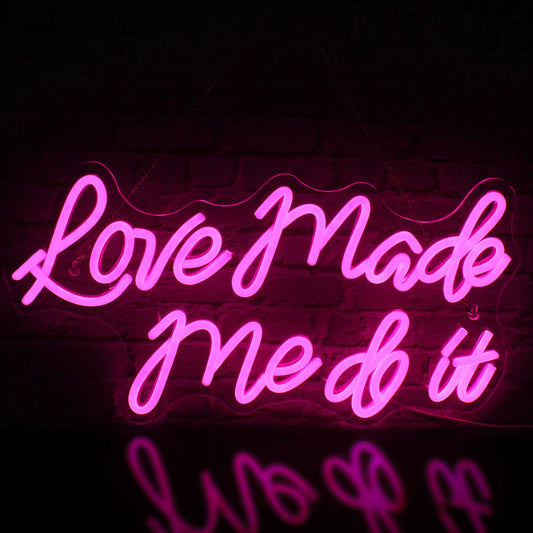 The image features a vibrant LED neon sign displaying the words "Love Made Me Do It" in a stylish cursive font.