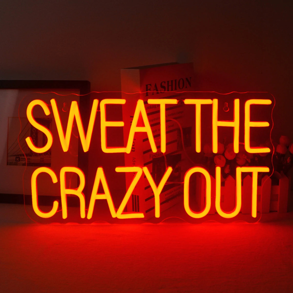 A vibrant LED neon sign displaying the phrase "Sweat The Crazy Out" in a playful cursive font.