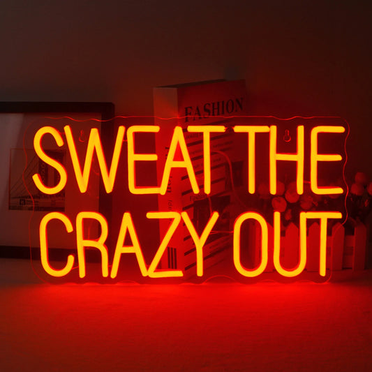 A vibrant LED neon sign displaying the phrase "Sweat The Crazy Out" in a playful cursive font.