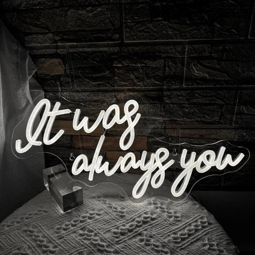 A imagem apresenta uma vibrante placa de LED neon exibindo as palavras "It Was Always You" em uma fonte cursiva e estilosa.