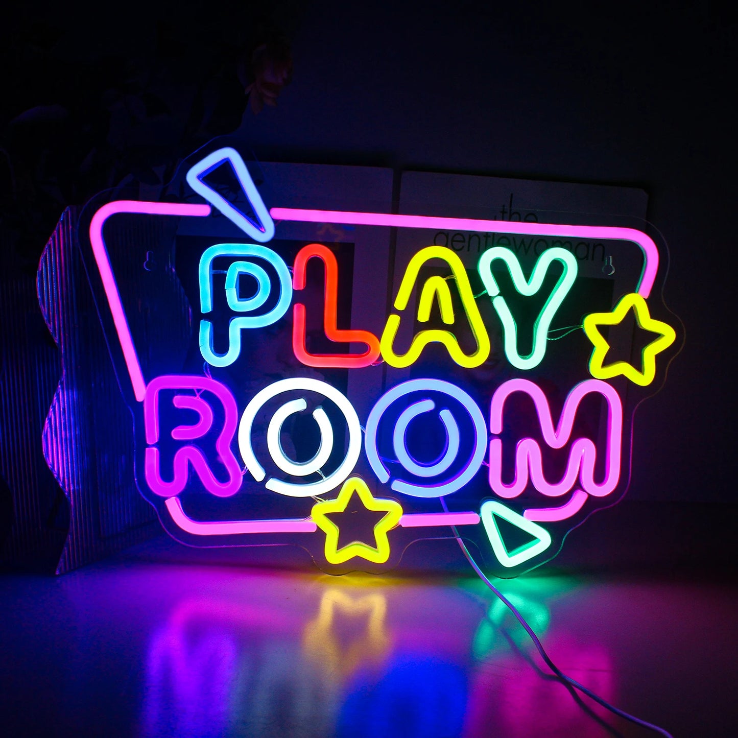 The image features a vibrant LED neon sign that reads "Play Room" in bright, playful colors.