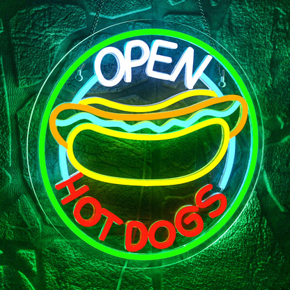 The image features a brightly lit LED neon sign displaying the words "Open Hot Dogs" in a playful, retro font.