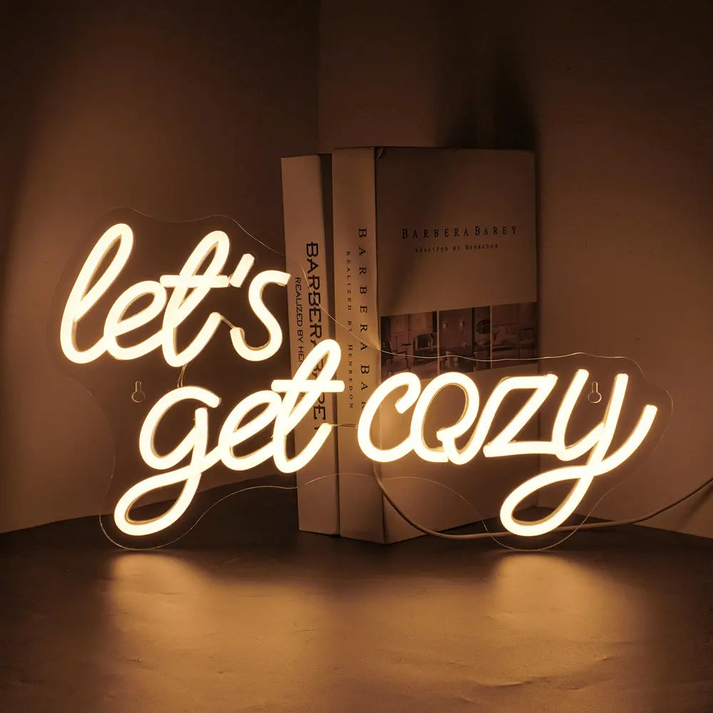 A imagem apresenta uma vibrante placa de LED neon exibindo a frase "Vamos nos aconchegar" em uma fonte calorosa e acolhedora.