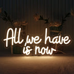 A imagem exibe uma placa de LED neon feita à mão com as palavras "All We Have Is Now" em letras vibrantes e luminosas.