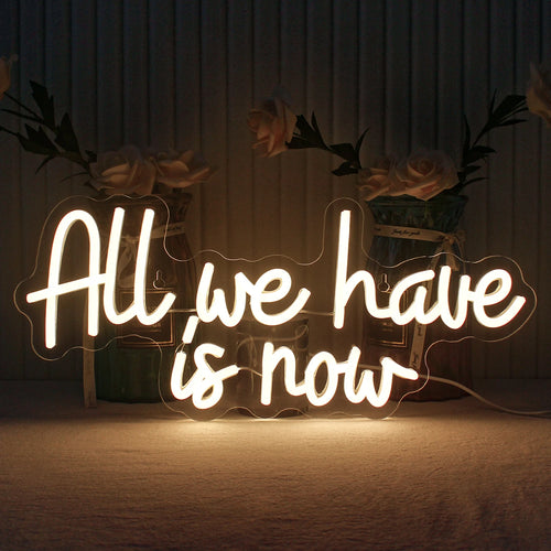 A imagem exibe uma placa de LED neon feita à mão com as palavras "All We Have Is Now" em letras vibrantes e luminosas.