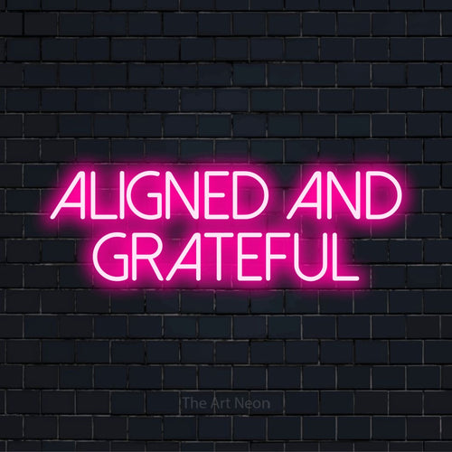 "Aligned And Grateful" script-style LED neon sign on a black brick wall