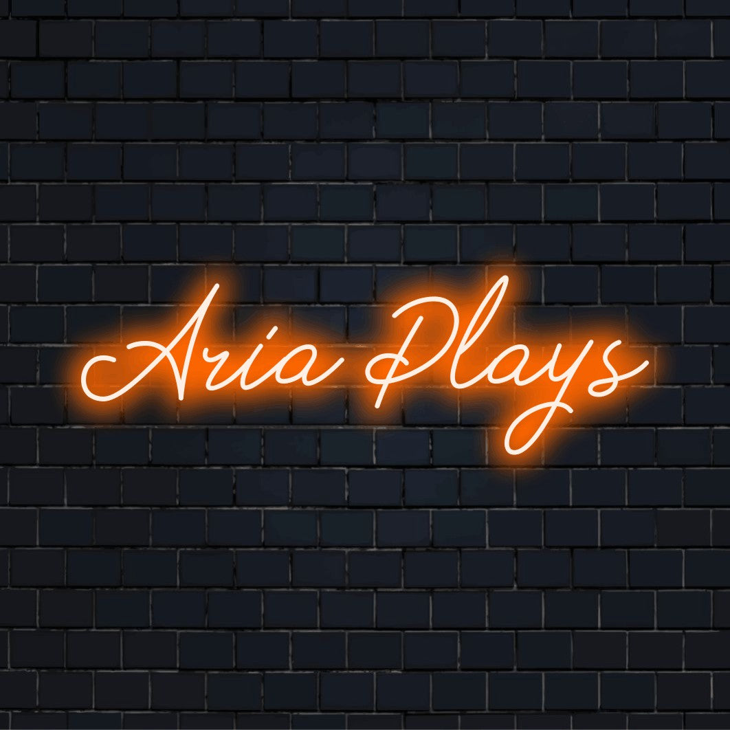 Aria Plays Custom Name Neon Sign, bright neon lettering on dark brick background