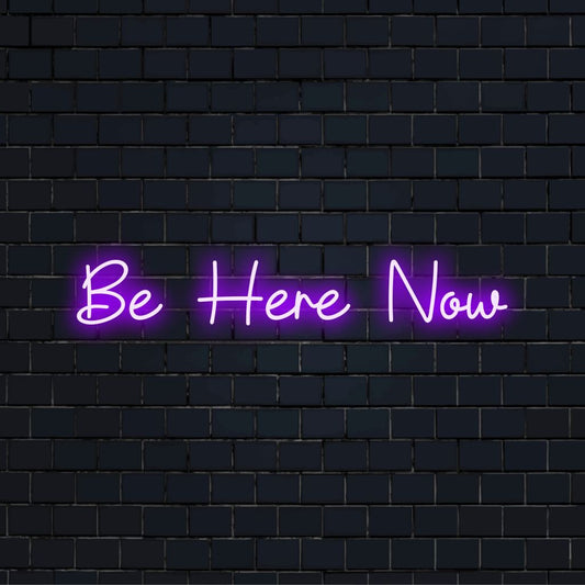 Be Here Now LED Neon Sign, glowing lettering on dark brick wall