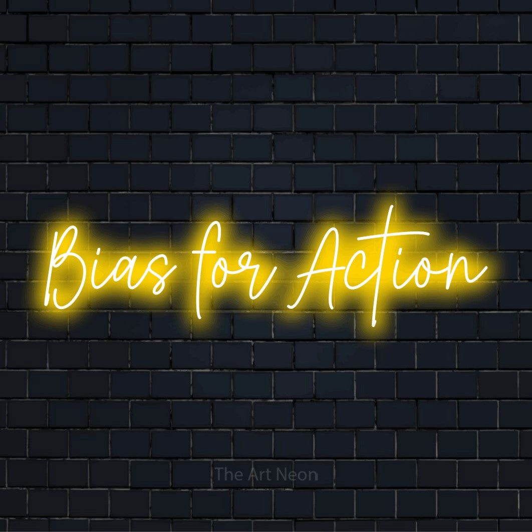 "Bias For Action" script-style LED neon sign on a black brick wall
