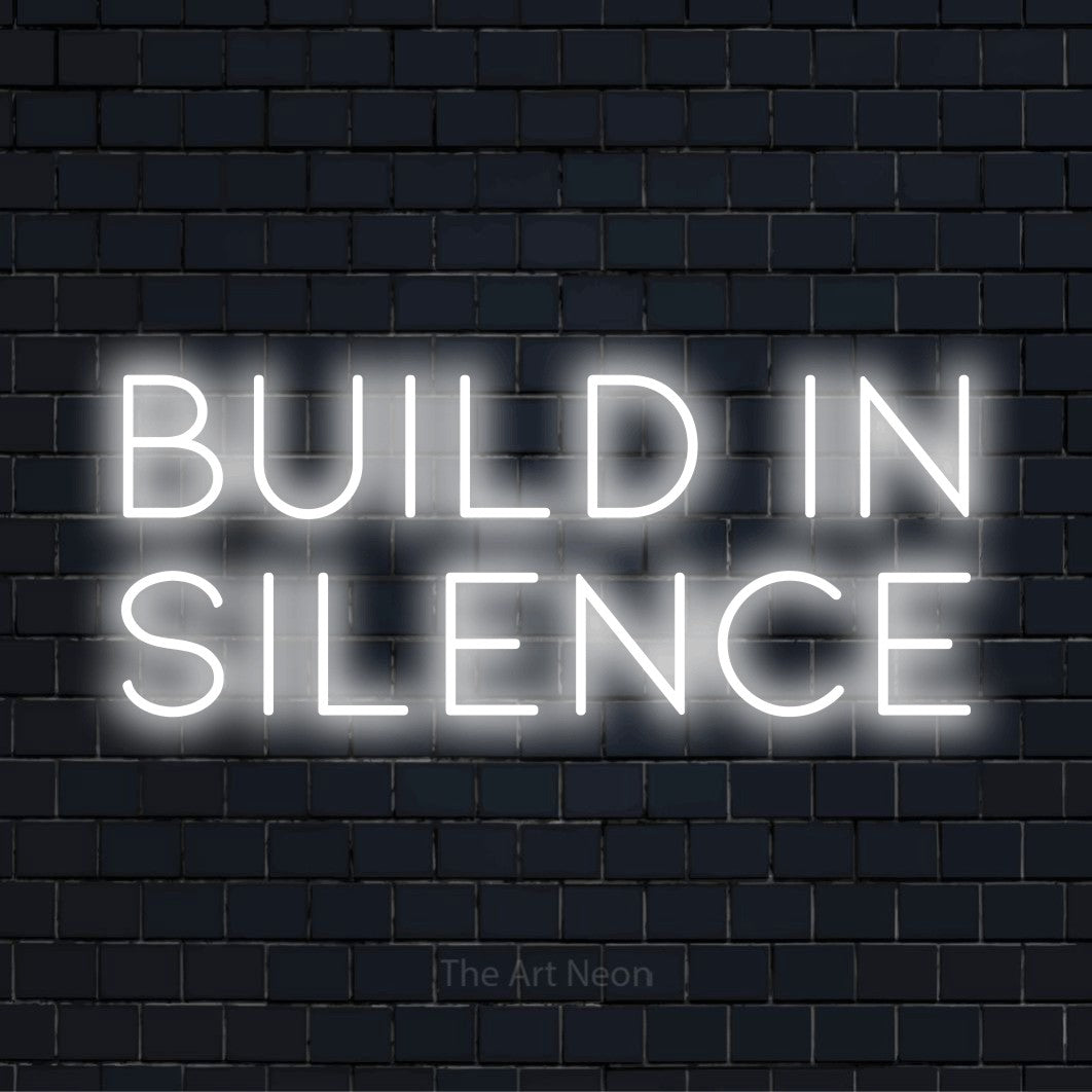 "Build In Silence" LED neon sign on a black brick wall
