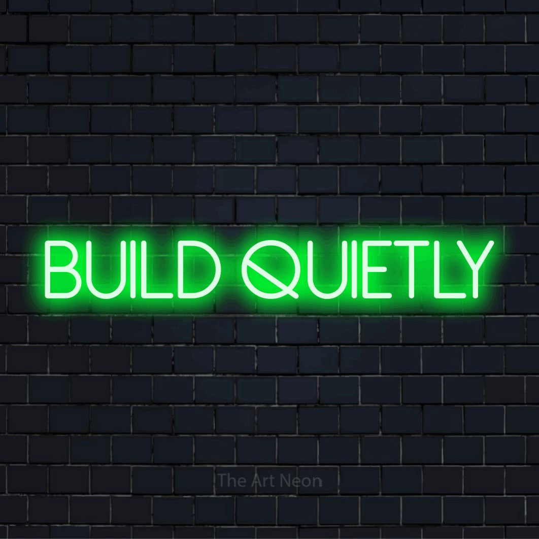 "Build Quietly" script-style LED neon sign on a black brick wall