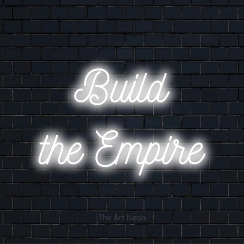 "Build The Empire" script-style LED neon sign on a black brick wall